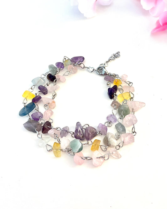 Surprenant bracelet à trois rangs, fait d'une rangée de pierre naturelle d'améthyste montée sur chaine, d'une rangée de fluorite montée sur chaine, et d'un troisième rang de pierres de quartz rose. La synergie de ces trois pierres semi-précieuses favorise l'amour de soi et aide à rétablir l'équilibre émotionnel.